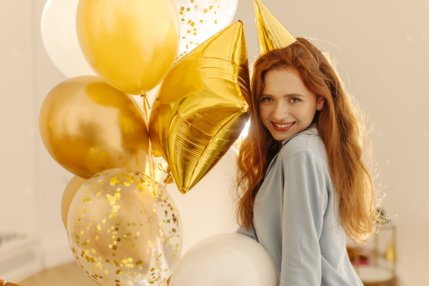 Ein energisches junges Mädchen, das auf einer Geburtstagsfeier einen Haufen goldener Luftballons hält