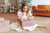 Kleines Mädchen mit einem weißes Kleid sitzt auf dem Boden und hält Geschenk